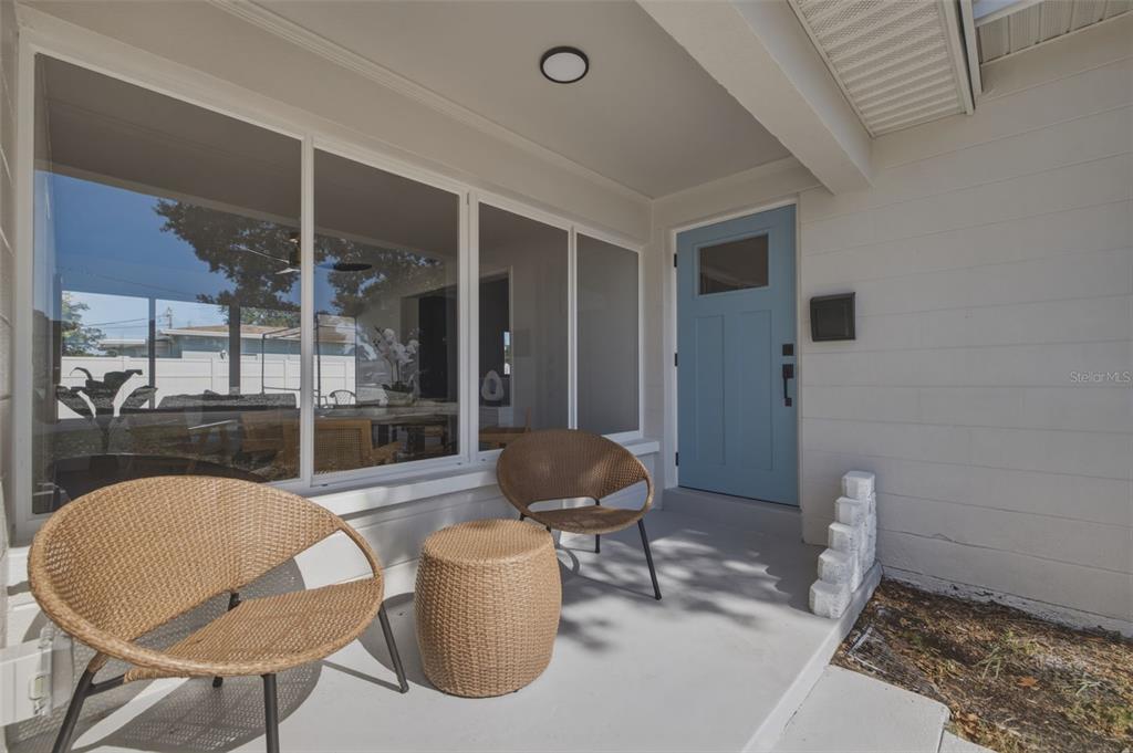 A covered front porch features two wicker chairs, a matching side table, and a blue door — 2465 38TH STREET N, ST PETERSBURG, FL