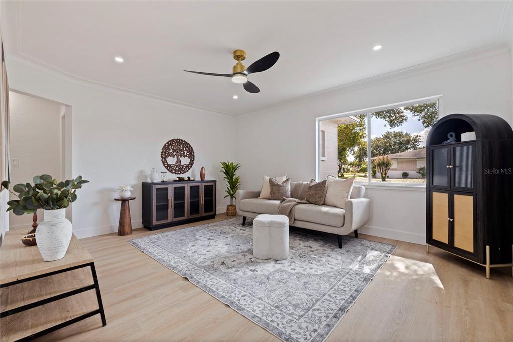 A living room features light wood flooring, a grey area rug, a sofa, and black furniture — 2465 38TH STREET N, ST PETERSBURG, FL
