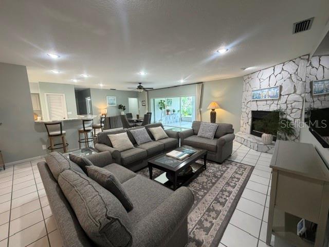 A living room with gray sofas, a stone fireplace, and tile flooring opens to a patio — 2241 WINTERSET ROAD, WINTER HAVEN, FL