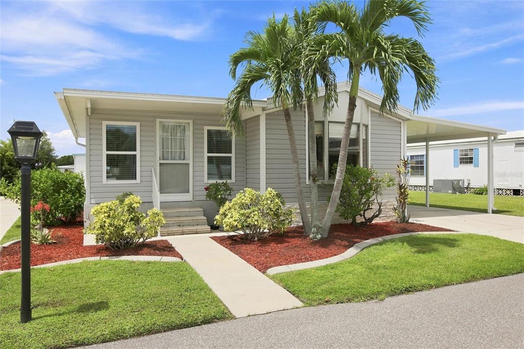 A light gray manufactured home features a palm tree, a concrete walkway, and a carport — 238 EGRET, PUNTA GORDA, FL