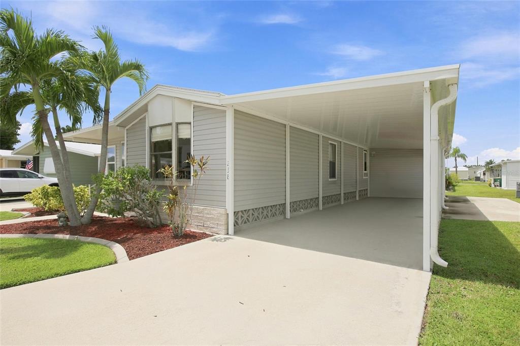 A light gray manufactured home features a long concrete carport and a landscaped front yard — 238 EGRET, PUNTA GORDA, FL