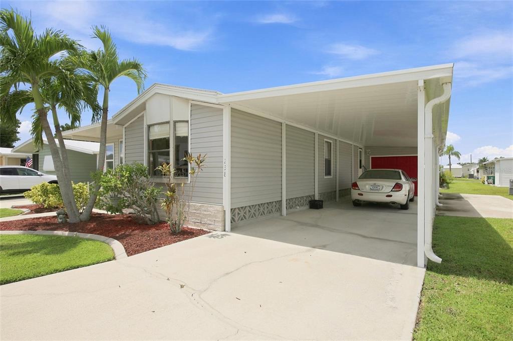 A light gray manufactured home features a concrete driveway, a covered carport, and palm trees — 238 EGRET, PUNTA GORDA, FL