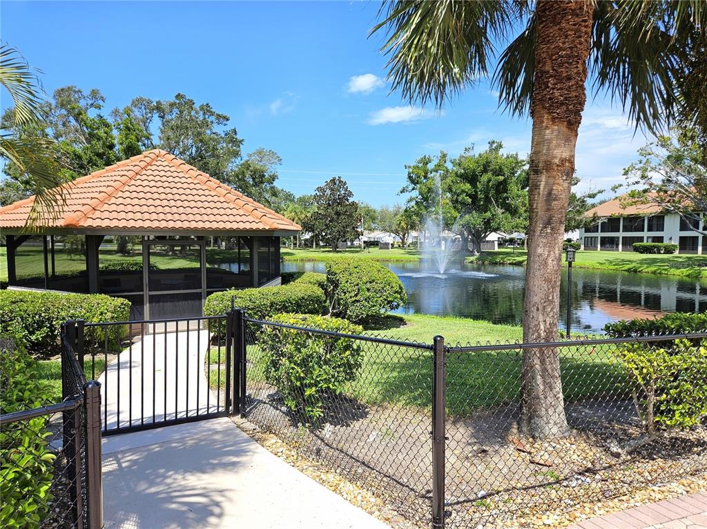 A gazebo sits beside a pond with a fountain, enclosed by a black metal fence — 756 AVENIDA ESTANCIA UNIT 162, VENICE, FL