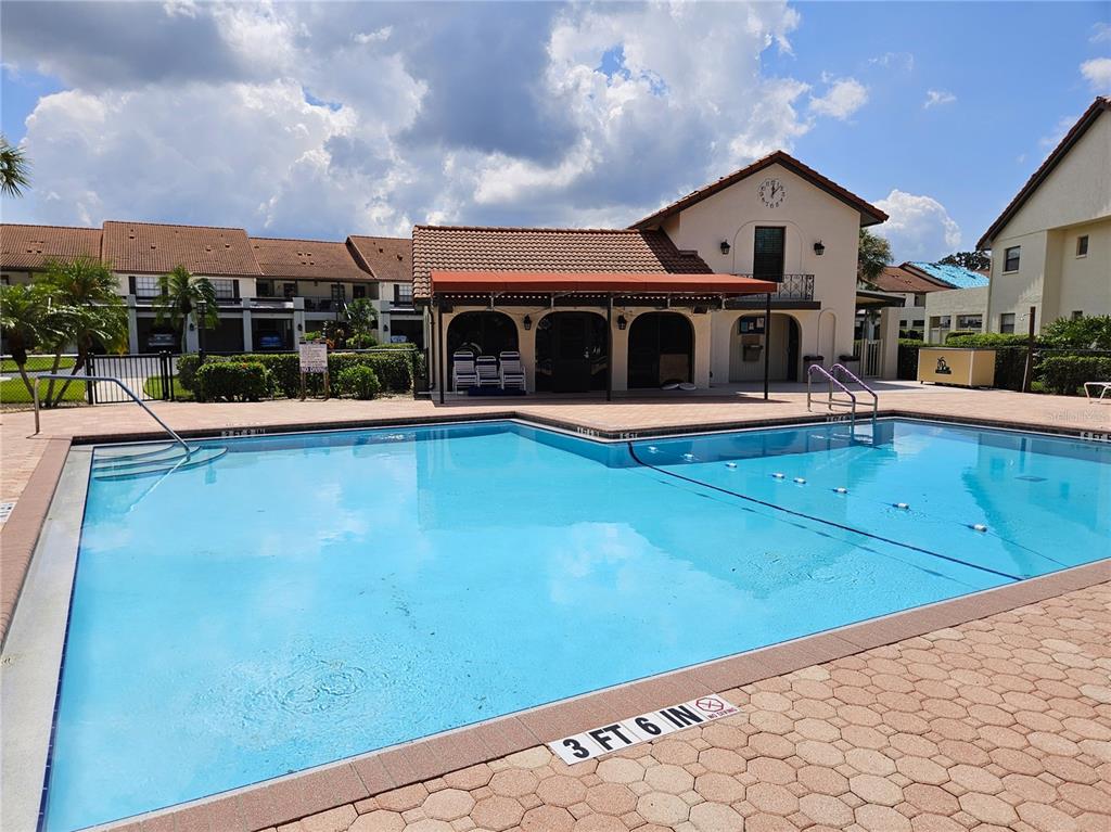 A swimming pool with a depth marker sits in front of a community clubhouse building — 756 AVENIDA ESTANCIA UNIT 162, VENICE, FL