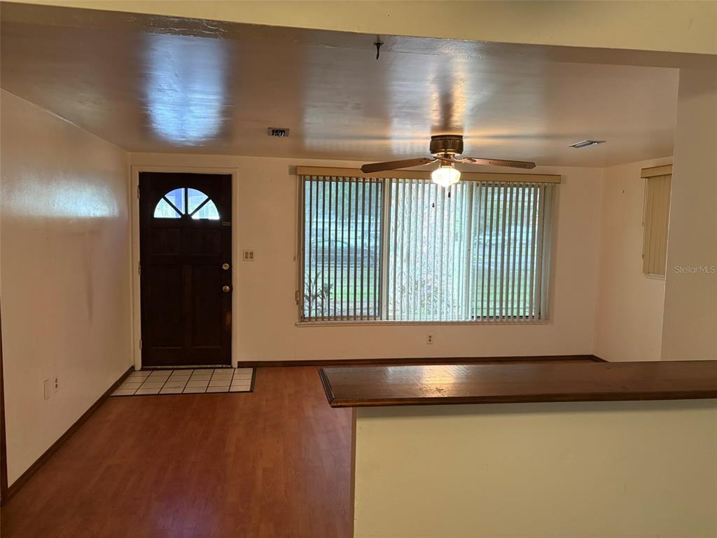 An interior view shows a living area with wood-look flooring, a ceiling fan, and front door — 671 DEXTER DRIVE, DUNEDIN, FL
