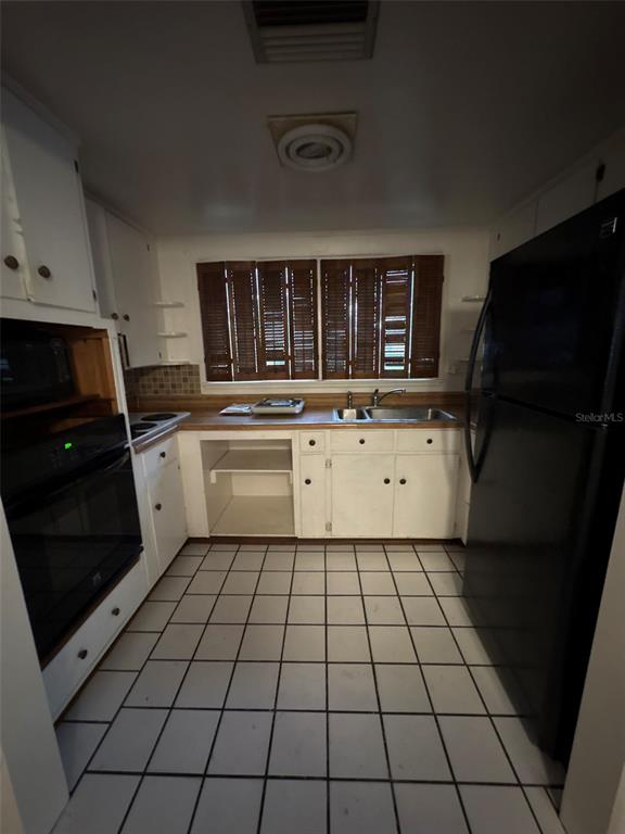 A kitchen features white cabinets, a black refrigerator, a black oven, and white tiled flooring — 671 DEXTER DRIVE, DUNEDIN, FL
