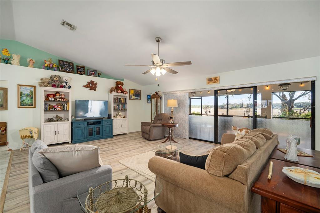A living room features light wood-look flooring, a vaulted ceiling, and a sliding glass door — 1472 IVYDALE ROAD, SPRING HILL, FL