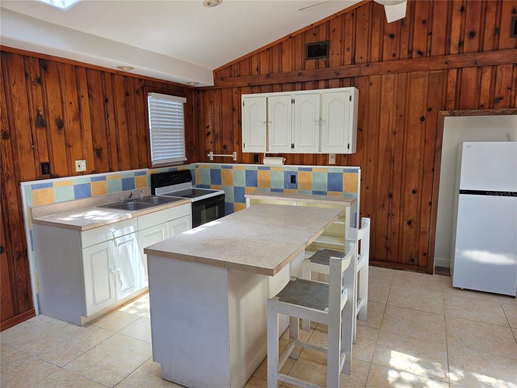 A kitchen features wood-paneled walls, white cabinetry, a central island, and a tiled backsplash — 5023 27TH AVENUE S, GULFPORT, FL
