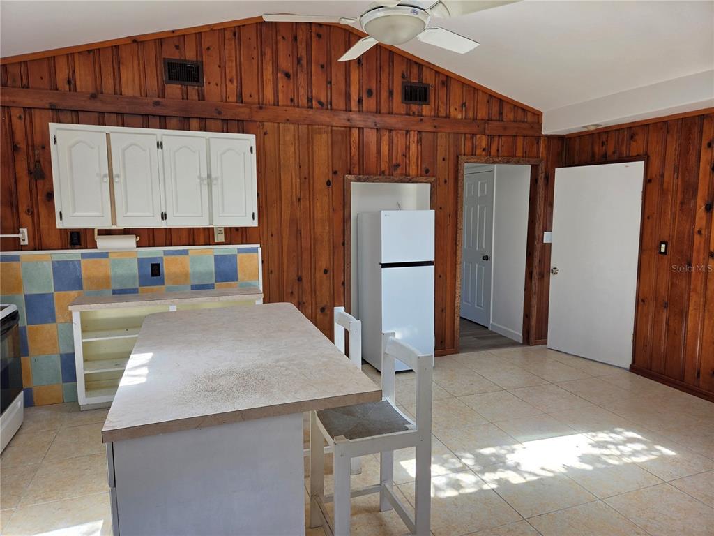 A kitchen with wood-paneled walls, a tiled backsplash, a central island, and white cabinets — 5023 27TH AVENUE S, GULFPORT, FL