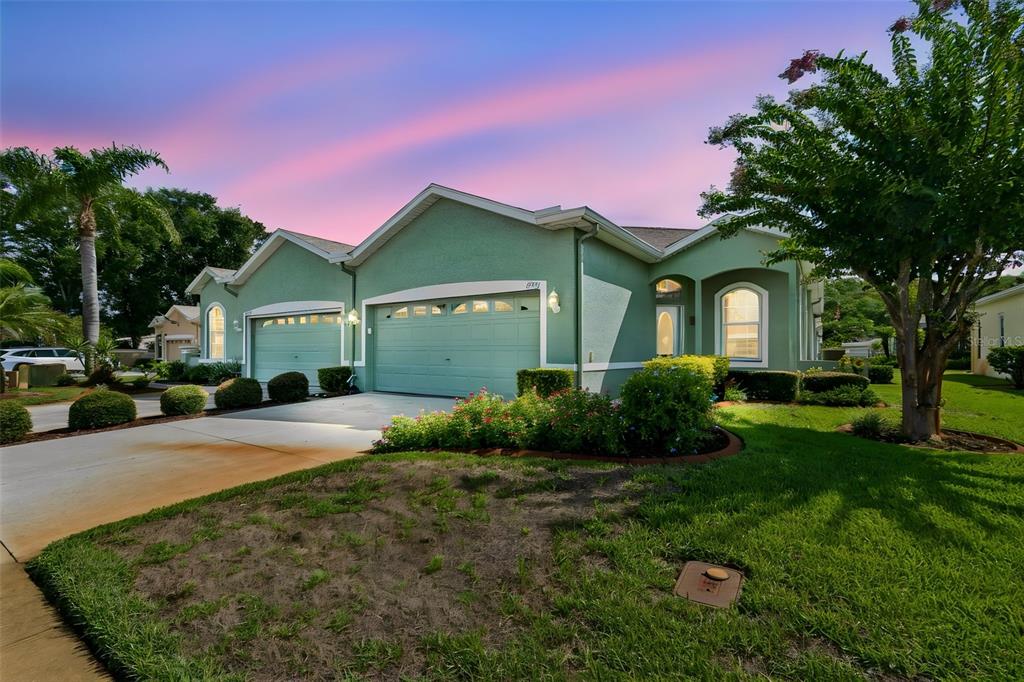 A single-story green house with a three-car garage and a landscaped front yard at sunset — 12154 PUTTER GREEN COURT, NEW PORT RICHEY, FL