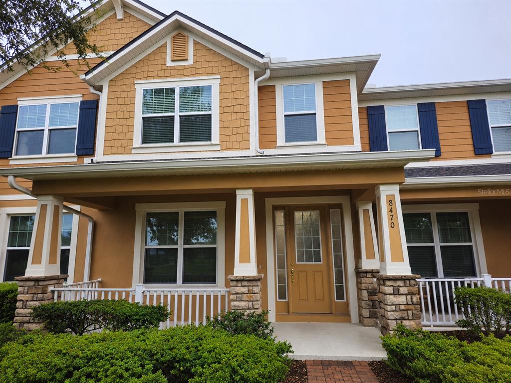 A two-story house exterior features tan siding, stone accents, a front porch, and blue shutters — 8470 IRON MOUNTAIN TRAIL, WINDERMERE, FL