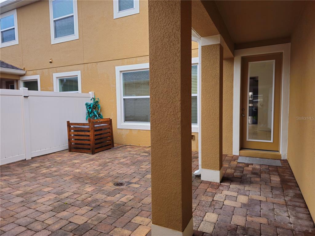 A paved patio area features a covered porch, a wooden privacy screen, and a glass door — 8470 IRON MOUNTAIN TRAIL, WINDERMERE, FL