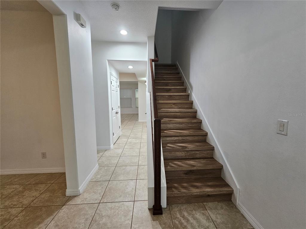A staircase with wood-look treads and a dark railing sits beside a tiled hallway — 8470 IRON MOUNTAIN TRAIL, WINDERMERE, FL