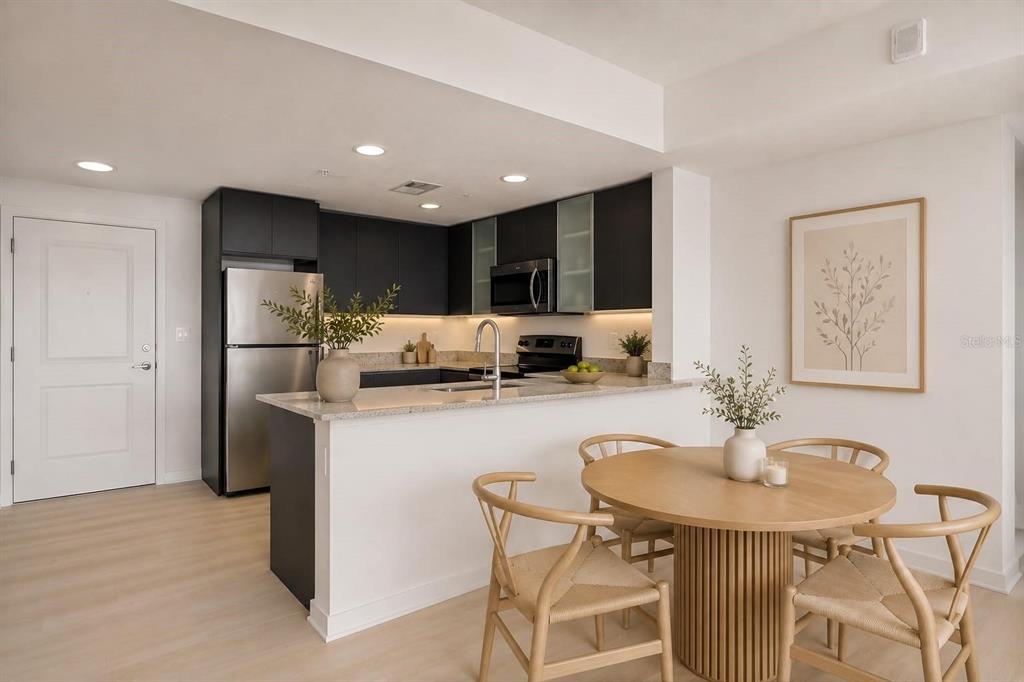 A kitchen with dark cabinets and stainless steel appliances overlooks a dining area with wood furniture — 5563 MILLENIA PARK BOULEVARD UNIT 401, ORLANDO, FL