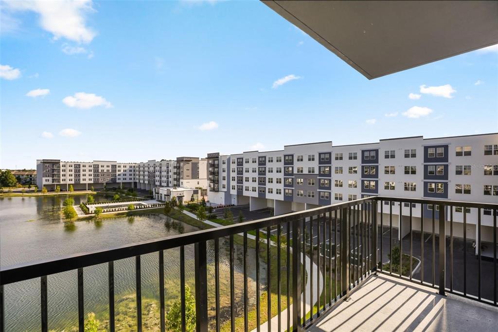 A balcony view overlooking a pond and modern apartment buildings under a blue sky — 5563 MILLENIA PARK BOULEVARD UNIT 401, ORLANDO, FL