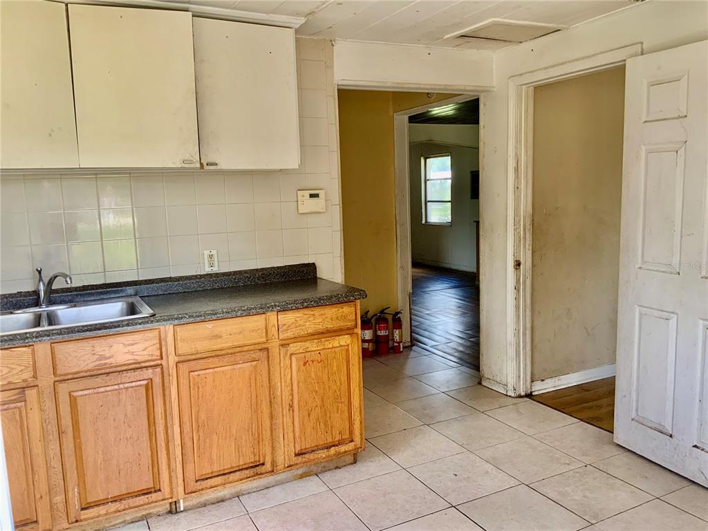 A kitchen with wooden cabinets, a double sink, tiled backsplash, and a doorway to another room — 2118 1ST AVENUE E, PALMETTO, FL
