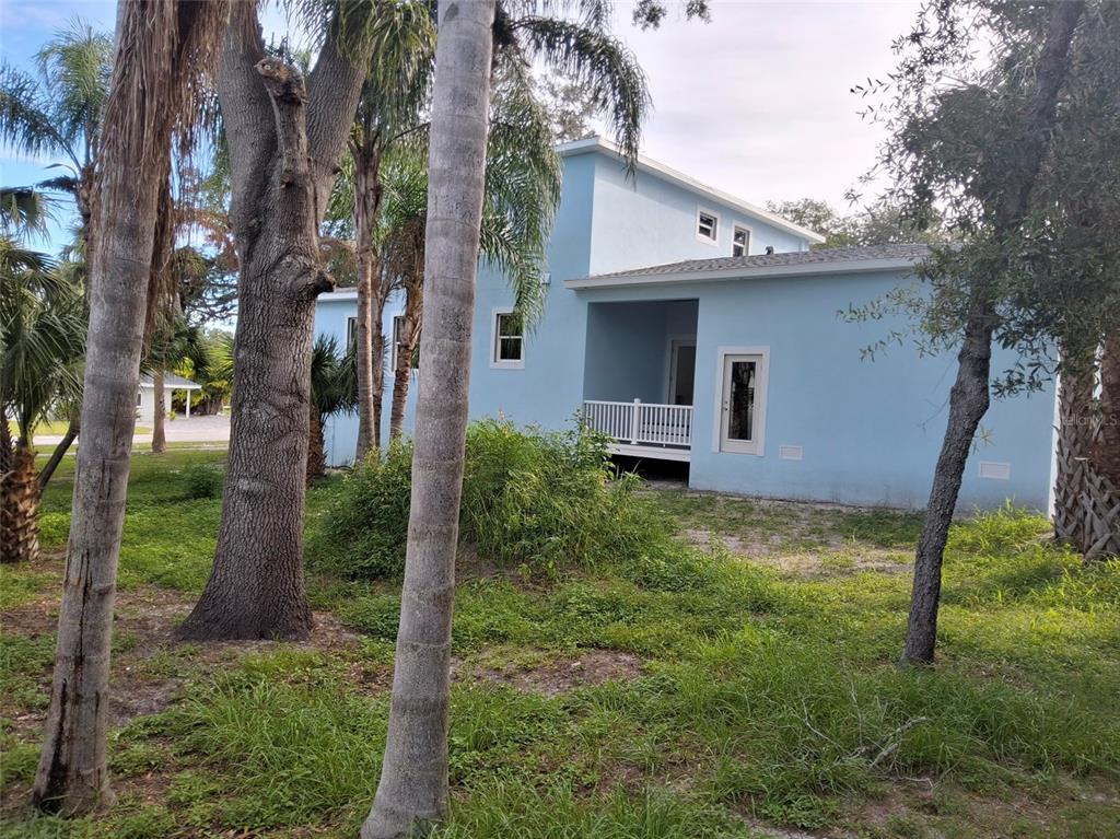 A blue two-story house stands behind several palm trees in a grassy, wooded yard — 383 GEORGIA AVENUE, CRYSTAL BEACH, FL
