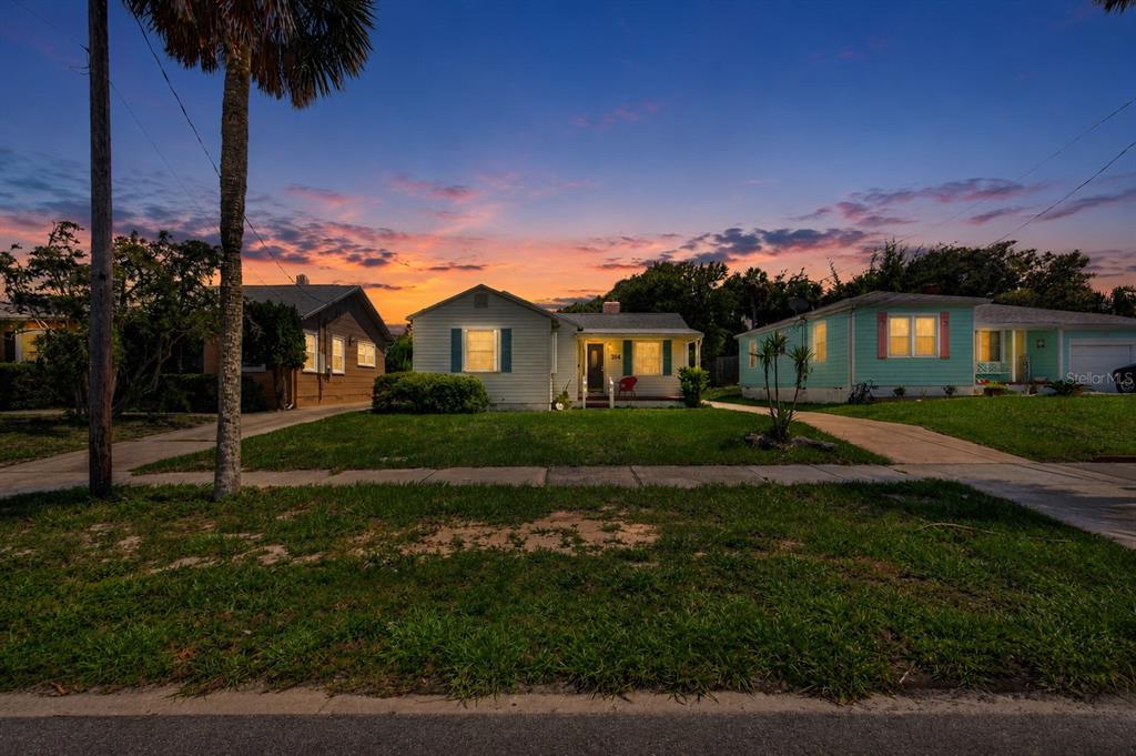Three single-story houses sit side-by-side along a street under a colorful sunset sky — 314 REVILO BOULEVARD, DAYTONA BEACH, FL