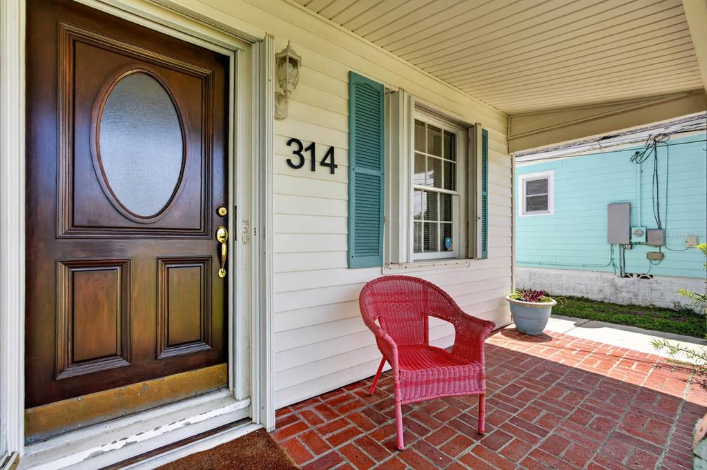 A red wicker chair sits on a brick porch next to a wooden front door — 314 REVILO BOULEVARD, DAYTONA BEACH, FL