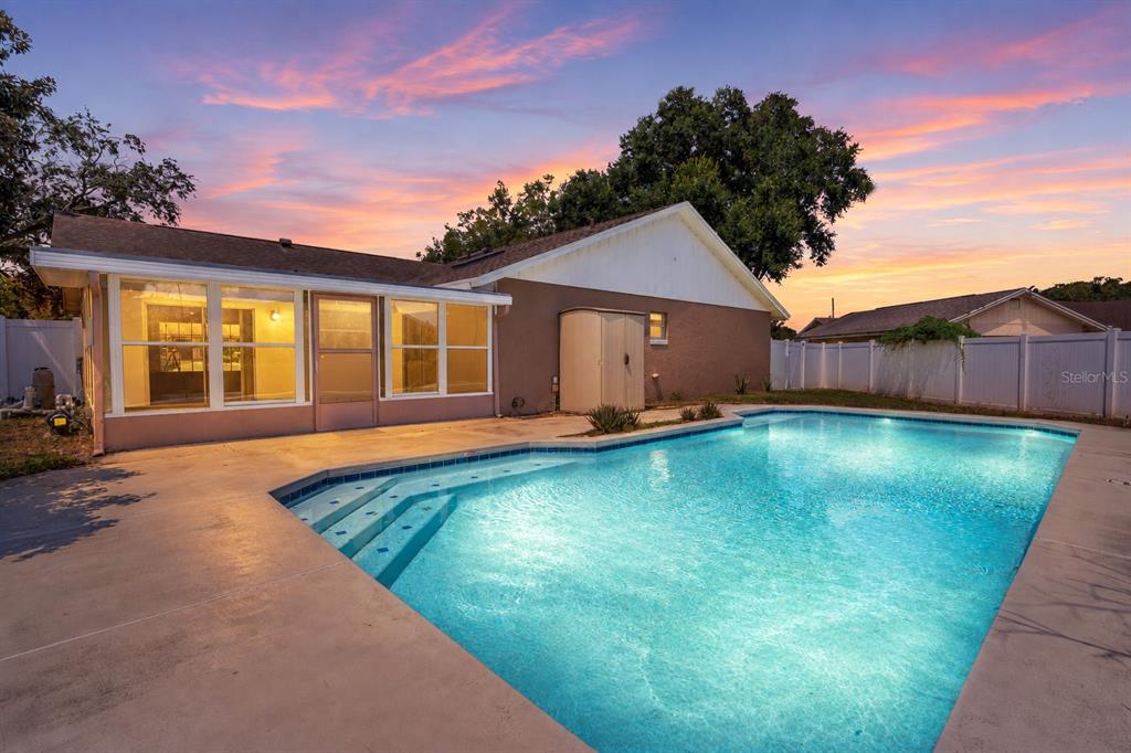 A backyard swimming pool with a concrete deck sits behind a house at sunset — 8971 ANGELICA DRIVE, ORLANDO, FL