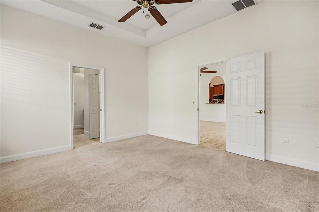 A carpeted bedroom features a tray ceiling with a fan and two open doorways — 314 TERRANOVA BOULEVARD, WINTER HAVEN, FL