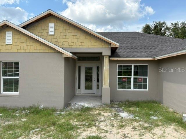 The exterior of a single-story house features gray stucco walls, tan shingle siding, and a roof — 6734 SW 179TH AVENUE ROAD, DUNNELLON, FL