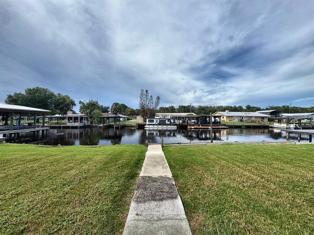 A concrete walkway leads through a grassy lawn to a canal with several boat docks — 1636 JUNO TRAIL, ASTOR, FL
