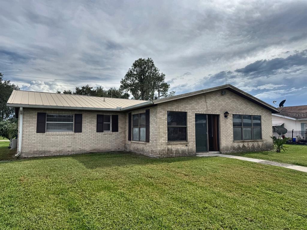 A single-story brick house with a metal roof and a front lawn under a cloudy sky — 1636 JUNO TRAIL, ASTOR, FL