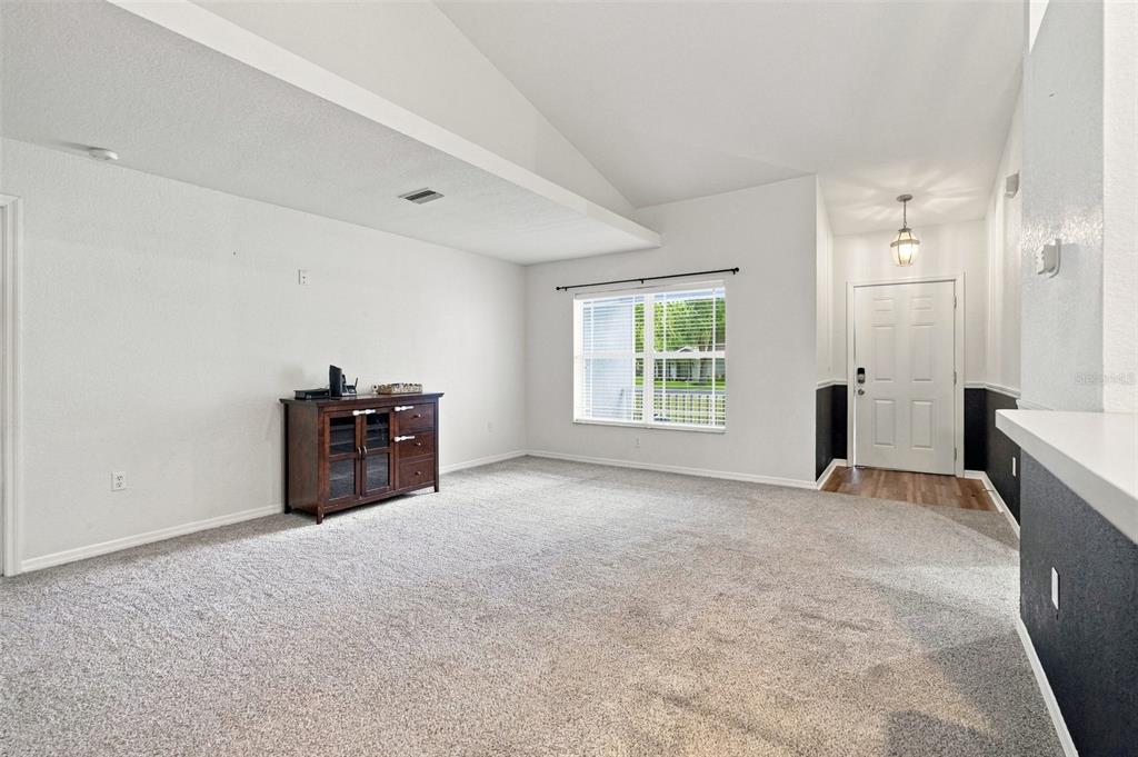 A living room with gray carpet, white walls, a vaulted ceiling, and a front entryway — 10041 KIMBROUGH DRIVE, BROOKSVILLE, FL