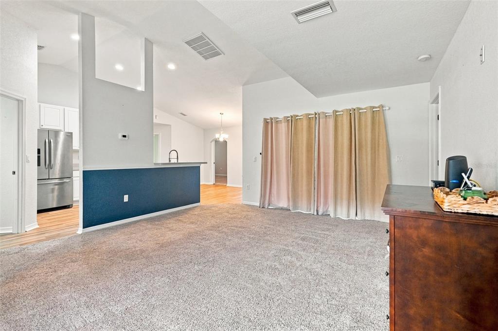 A living room with gray carpet, a blue half-wall, and beige curtains covering a window — 10041 KIMBROUGH DRIVE, BROOKSVILLE, FL