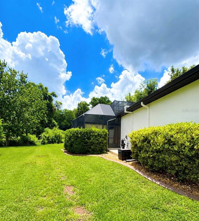 A view of a house exterior featuring a screened-in pool enclosure and landscaped bushes — 30 EGRET TRAIL, PALM COAST, FL