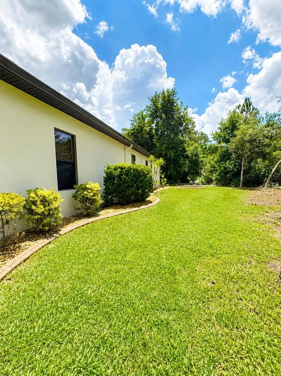 A side view of a house exterior with a lawn, landscaping, and a blue sky — 30 EGRET TRAIL, PALM COAST, FL