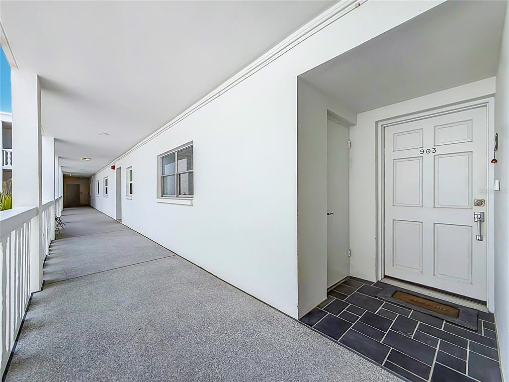 An outdoor apartment hallway features a white door labeled 903 and a gray tiled entryway — 4950 GULF BOULEVARD UNIT 903, ST PETE BEACH, FL
