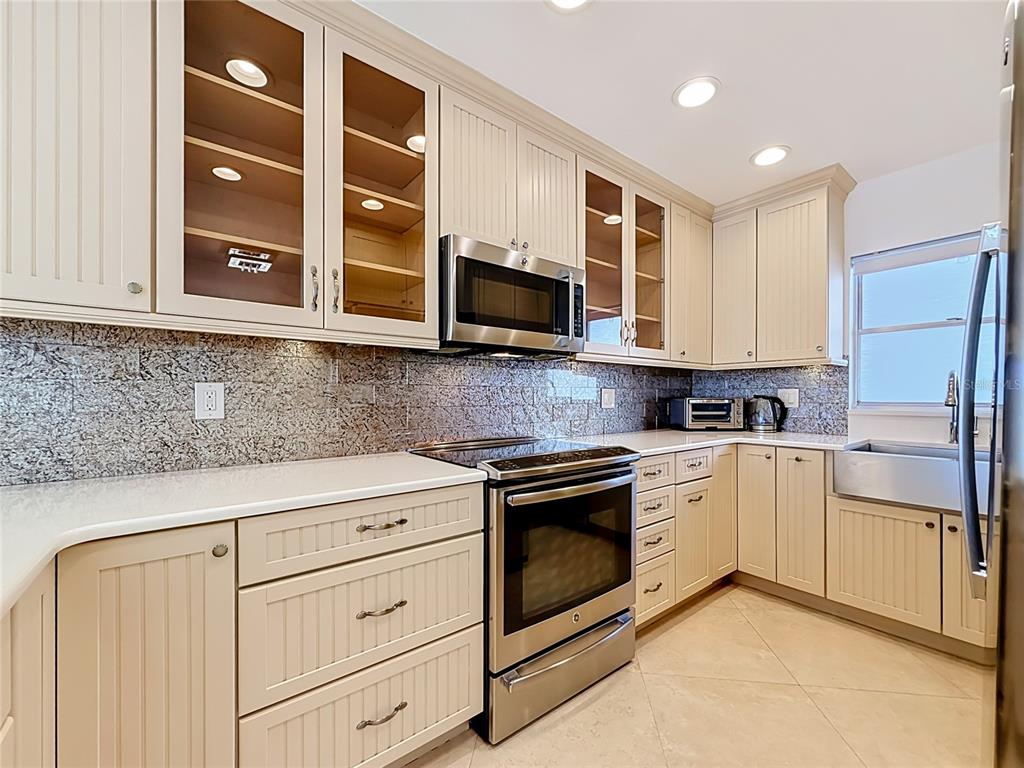 A kitchen features cream-colored beadboard cabinets, stainless steel appliances, and a granite tile backsplash — 4950 GULF BOULEVARD UNIT 903, ST PETE BEACH, FL