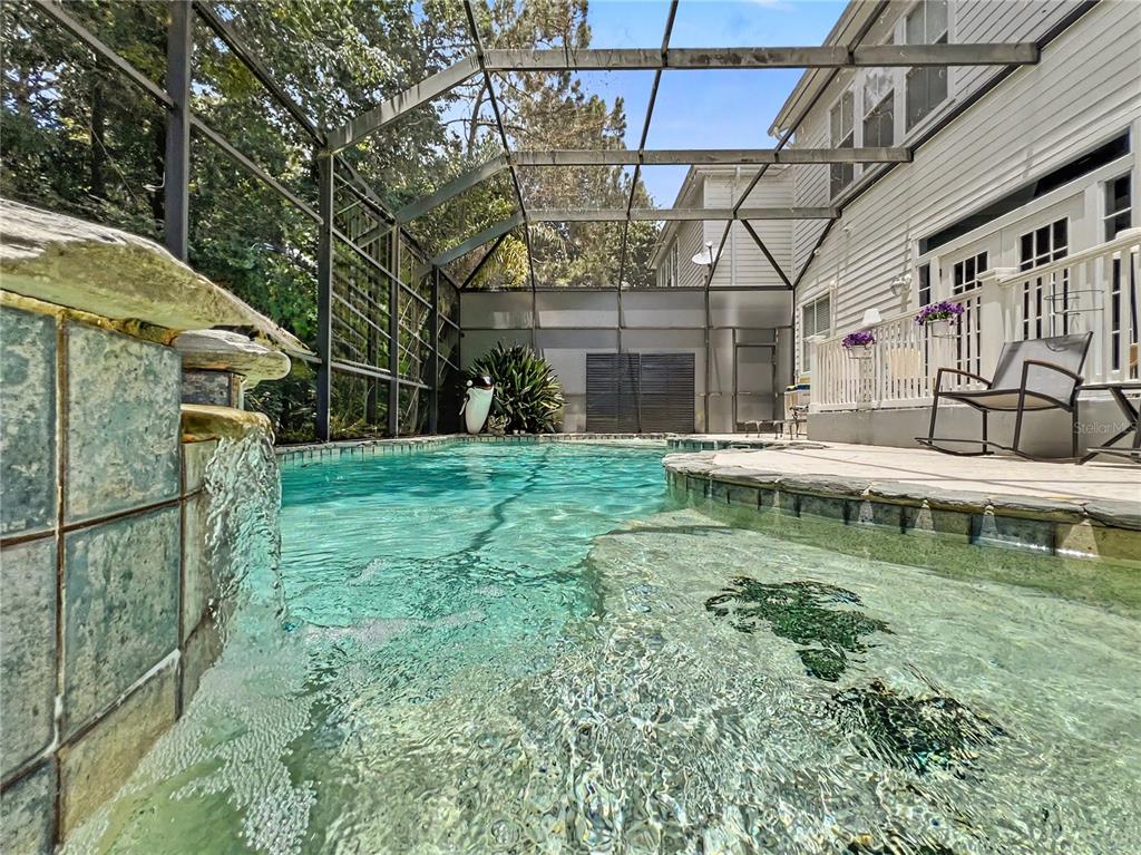 A screened-in swimming pool with a waterfall feature and a patio area next to a house — 816 RUNNER OAK STREET, CELEBRATION, FL