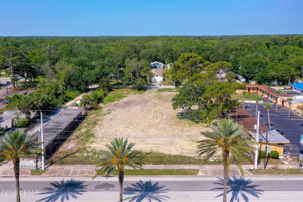 An aerial view shows a vacant, fenced-in lot situated between two existing commercial buildings — 670 S YONGE STREET, ORMOND BEACH, FL