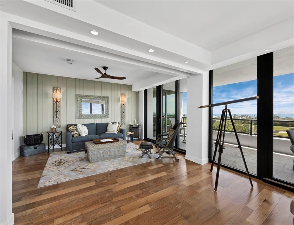 A living room features hardwood floors, a blue sofa, and a telescope facing a balcony — 535 SANCTUARY DRIVE UNIT A603, LONGBOAT KEY, FL