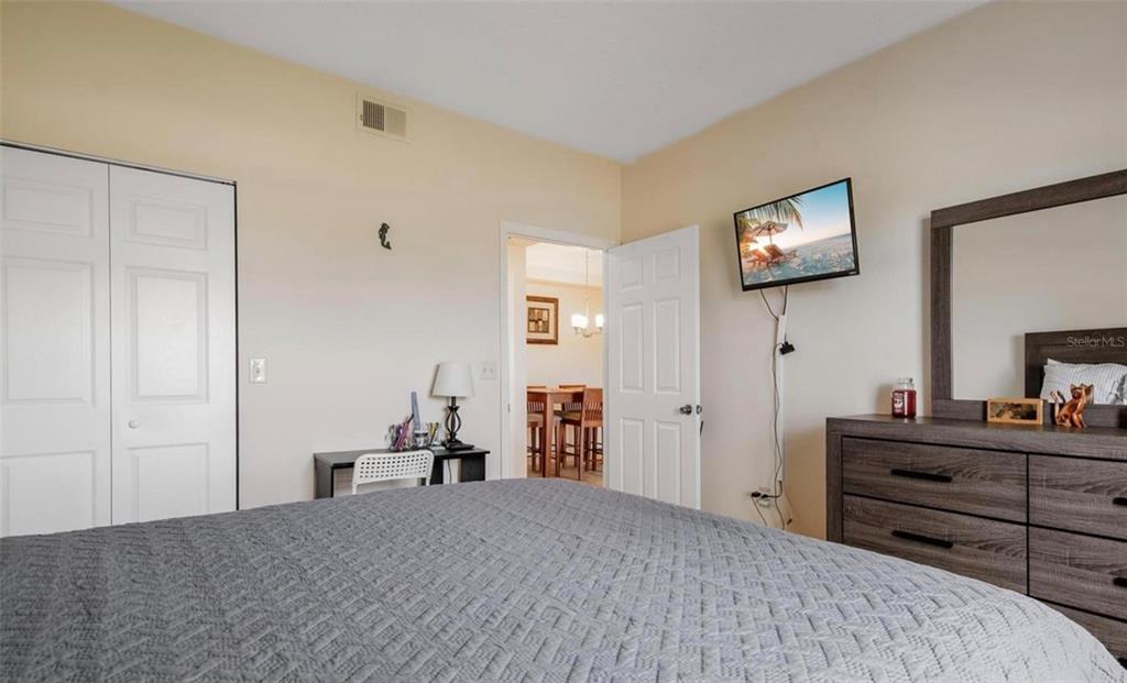 A bedroom features a gray bedspread, a dresser with a mirror, and a wall-mounted television — 11490 VILLA GRAND UNIT 221, FORT MYERS, FL