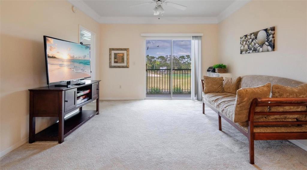 A living room with beige carpet, a wooden sofa, a television console, and a sliding door — 11490 VILLA GRAND UNIT 221, FORT MYERS, FL