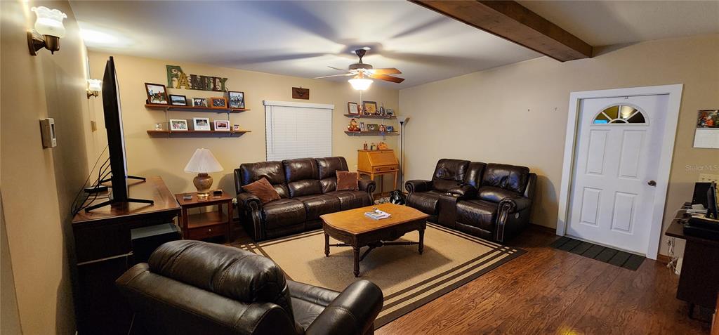 A living room features dark leather furniture, wood flooring, a ceiling fan, and a front door — 1190 S GOODMAN ROAD, CHAMPIONS GATE, FL