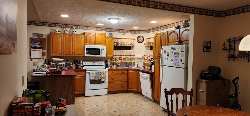 A kitchen features wood cabinets, white appliances, a peninsula, and a tiled floor — 1190 S GOODMAN ROAD, CHAMPIONS GATE, FL