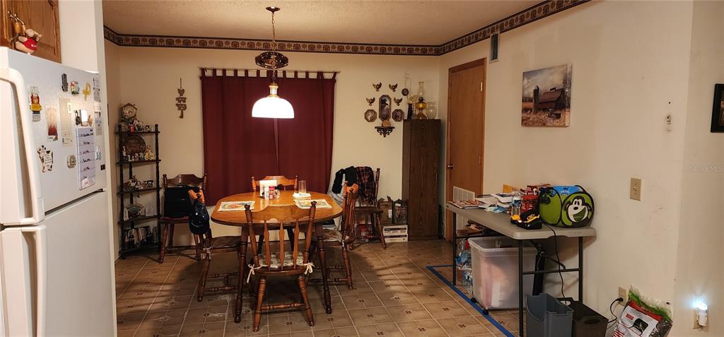 A dining area features a wooden table with chairs, a hanging light fixture, and tile flooring — 1190 S GOODMAN ROAD, CHAMPIONS GATE, FL