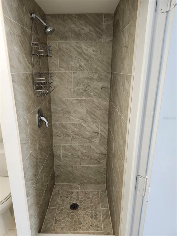 A walk-in shower features gray marble-look wall tiles and a hexagonal tile floor — 6144 SAPPHIRE DRIVE, NEW PORT RICHEY, FL