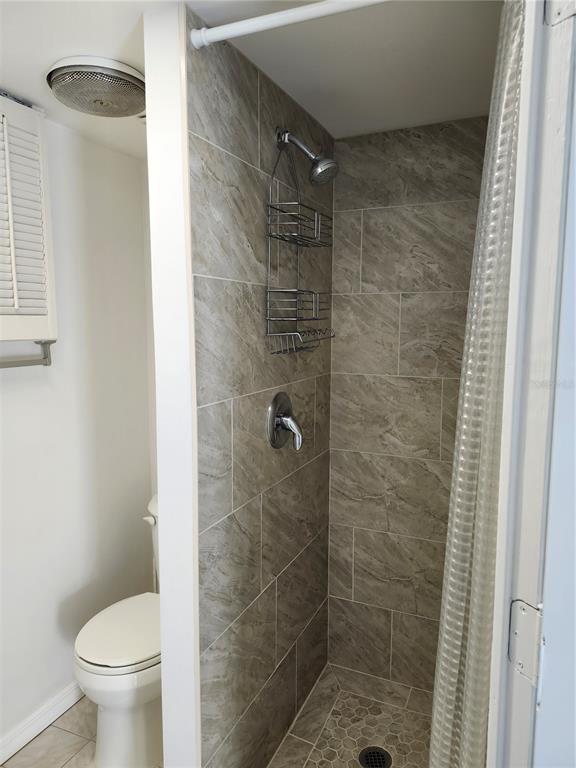 A bathroom features a tiled walk-in shower with a hanging caddy next to a toilet — 6144 SAPPHIRE DRIVE, NEW PORT RICHEY, FL