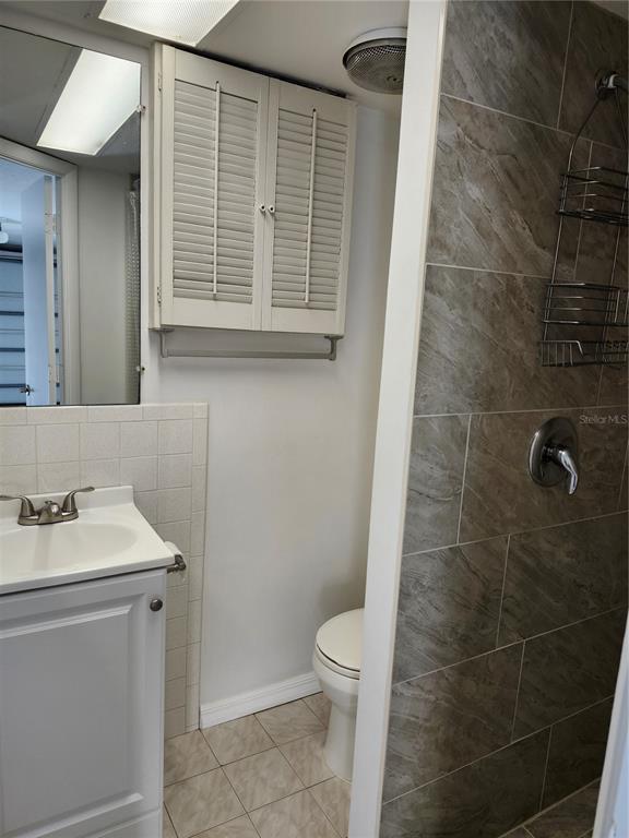 A bathroom features a white vanity, a toilet, a wall cabinet, and a tiled shower — 6144 SAPPHIRE DRIVE, NEW PORT RICHEY, FL