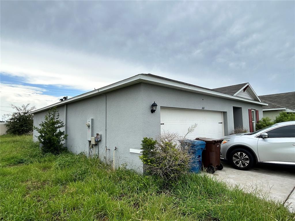 A gray stucco house exterior features a white garage door, a driveway, and overgrown grass — 364 BOARDWALK AVENUE, HAINES CITY, FL