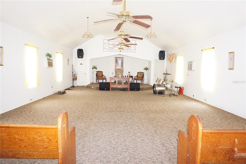 A church sanctuary features a carpeted floor, wooden pews, a raised stage, and ceiling fans — 12701 NW 38TH AVENUE, REDDICK, FL