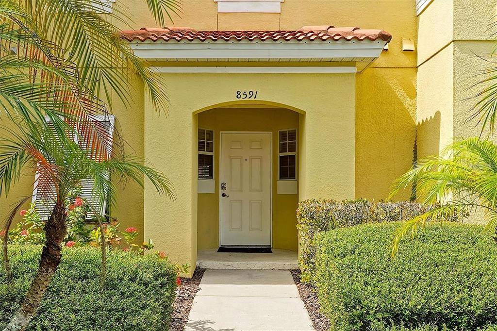 A yellow stucco building exterior features a covered entryway with a white door and landscaping — 8591 BAY LILLY LOOP, KISSIMMEE, FL