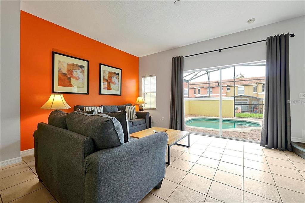 A living room with an orange accent wall, gray sofa, and sliding doors to a pool — 8591 BAY LILLY LOOP, KISSIMMEE, FL