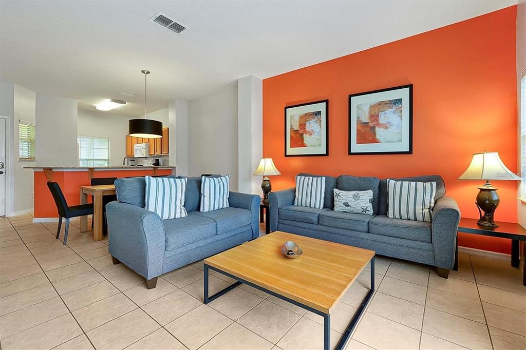 A living room features blue sofas, a wooden coffee table, and a bright orange accent wall — 8591 BAY LILLY LOOP, KISSIMMEE, FL